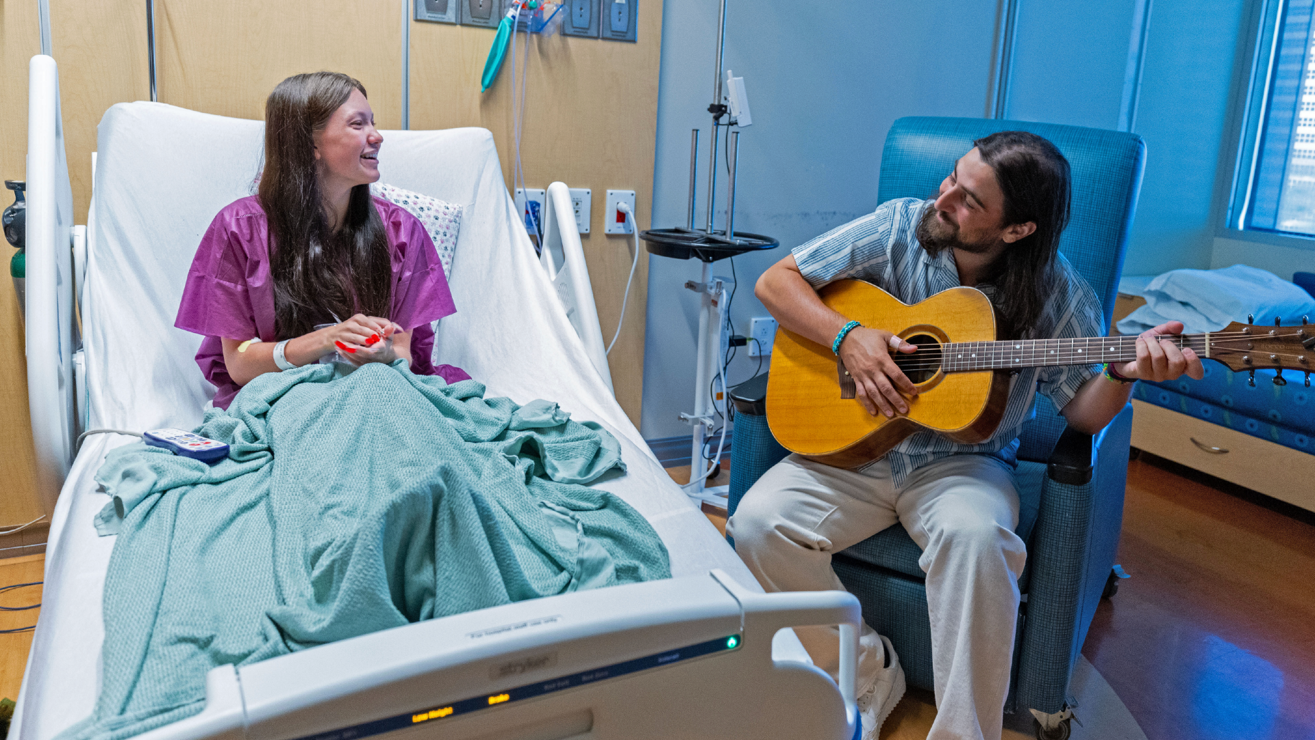 Noah Kahan playing guitar for a patient in a hospital setting